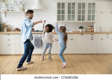 Caucasian father multi-racial school age daughters enjoy dance battle funny activity in modern new renovated kitchen spend active time together on weekend at home. Have fun, happy fatherhood concept - Powered by Shutterstock