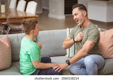 Caucasian father and son communicating using sign language while sitting on the couch at home. sign language learning concept - Powered by Shutterstock