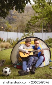 Caucasian father and son playing guitar together while sitting in a tent in the garden. fatherhood and love concept