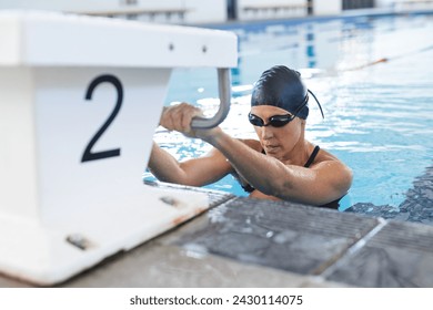 Caucasian female athlete swimmer prepares for a swim at an indoor pool. Her focused expression captures the intensity of competitive swimming. - Powered by Shutterstock