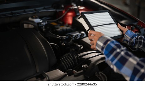 Caucasian female auto mechanic changes the engine air filter in the car.
