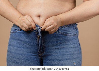 Caucasian female with big belly and overweighted sides trying to zip up blue jeans. Visceral fat. Body positive. Sudden weight gain. Tight little clothes. Need for wardrobe change.