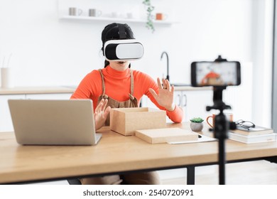 Caucasian female blogger unboxing new virtual reality headset for online audience. Young woman sharing engaging tech content from home office. Creative setup with laptop, smartphone, and modern desk. - Powered by Shutterstock