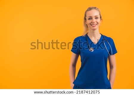 Caucasian female blonde nurse wearing scrubs standing confidently hands in pockets looking into camera smilng invitingly. Studio shot. . High quality photo