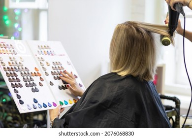 Caucasian Female Client And Asian Hairdresser, Hair Stylist In Beauty Salon Choosing Hair Color For Coloring, Dyeing On Palette In Catalog