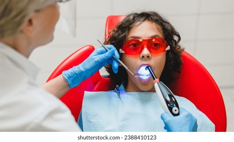 Caucasian female dentist orthodontist filling child boy`s tooth teeth while patient wearing red protective glasses during operation in stomatology hospital - Powered by Shutterstock