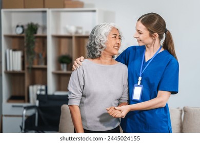 Caucasian female doctor assists in supporting an elderly Asian patient while they both sit on the sofa, ensuring comfort and stability during the interaction. - Powered by Shutterstock