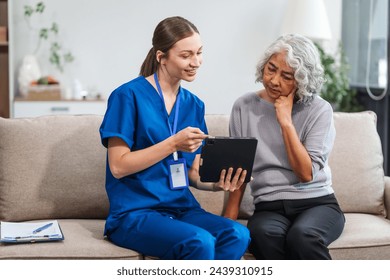 Caucasian female doctor conducts a check-up using a tablet device for an elderly Asian patient seated together on the sofa. - Powered by Shutterstock