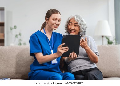 Caucasian female doctor conducts a check-up using a tablet device for an elderly Asian patient seated together on the sofa. - Powered by Shutterstock