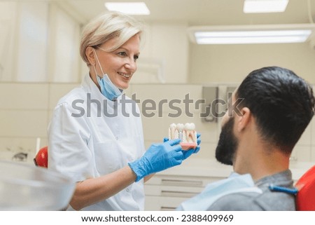 Caucasian female doctor dentist orthodontist showing explaining to a male patient dental teeth tooth root implantation, caries decay cure in clinic