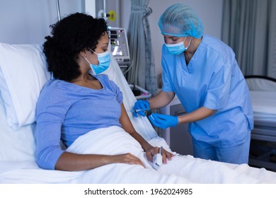 Caucasian Female Doctor In Hospital Wearing Face Mask Vaccinating African American Female Patient. Medical Professional At Work During Coronavirus Covid 19 Pandemic.