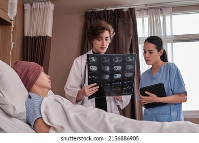 Caucasian Female Doctor In Uniform Diagnosis Explains X-ray Film With Asian Radiologist And Recovery Male Patient At Inpatient Room Bed In A Hospital Ward, Medical Clinic, Cancer Examination Consult.