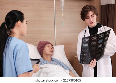 Caucasian Female Doctor In Uniform Diagnosis Explains X-ray Film With Asian Radiologist And Recovery Male Patient At Inpatient Room Bed In A Hospital Ward, Medical Clinic, Cancer Examination Consult.