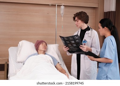 Caucasian Female Doctor In Uniform Diagnosis Explains X-ray Film With Asian Radiologist And Recovery Male Patient At Inpatient Room Bed In A Hospital Ward, Medical Clinic, Cancer Examination Consult.