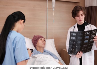 Caucasian Female Doctor In Uniform Diagnosis Explains X-ray Film With Asian Radiologist And Recovery Male Patient At Inpatient Room Bed In A Hospital Ward, Medical Clinic, Cancer Examination Consult.