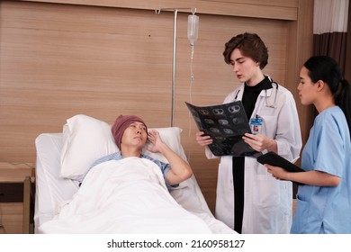 Caucasian Female Doctor In Uniform Diagnosis Explains X-ray Film With Asian Radiologist And Recovery Male Patient At Inpatient Room Bed In A Hospital Ward, Medical Clinic, Cancer Examination Consult.