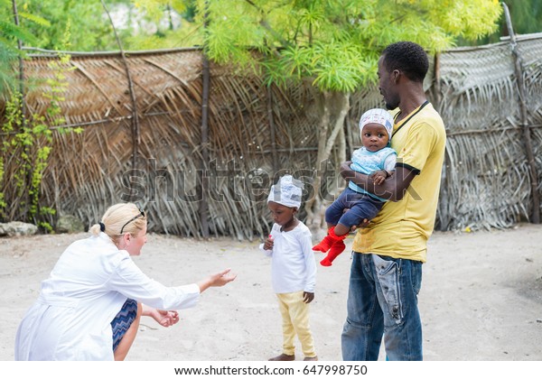 村に住むアフリカ系の黒人家族の一人を訪れ 幼い黒人女性と出会い 赤ちゃんを抱えた父親と出会う白人女性医師 赤ちゃんの顔に最もフォーカスを合わせる 浅い落書き の写真素材 今すぐ編集