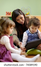 Caucasian female educator and little girls reading fairy tale on touch pad computer in kindergarten