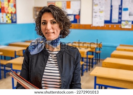 Caucasian female elementary teacher with brown short curly hair standing in an empty classroom. Waist up portrait view of real people. Educational background with copy space. Back to school concept.