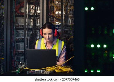 Caucasian female engineer wearing ear plugs using a laptop in computer server room. database server management and maintenance concept - Powered by Shutterstock