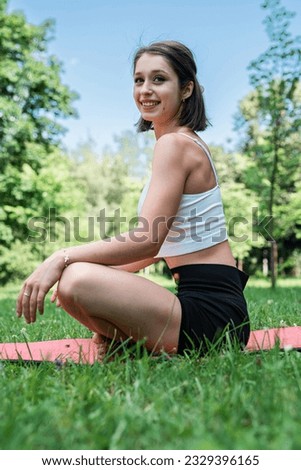Caucasian female fitness trainer practicing yoga or pilates on green grass in beautiful summer day.  Workout outdoors, healthy lifestyle 