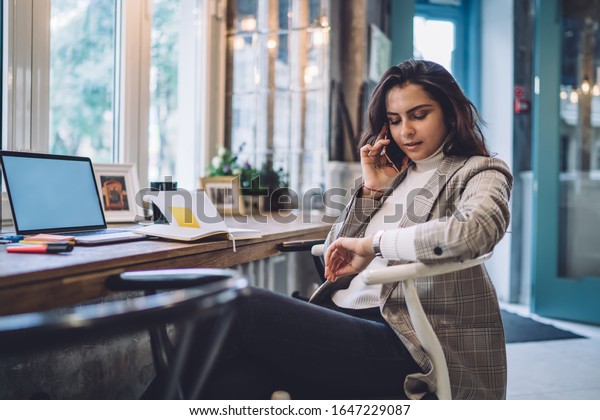 Caucasian female freelancer checking time on wearable\
wrist watch during time for remote work on blank laptop with copy\
space area for internet advertising, young woman talking via\
cellphone app