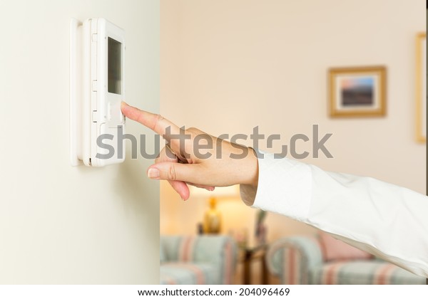 Female hand operating a thermostat in warm and welcoming modern home