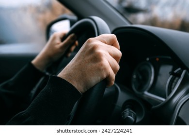 Caucasian female hands holding car steering wheel while driving through countryside landscape, selective focus