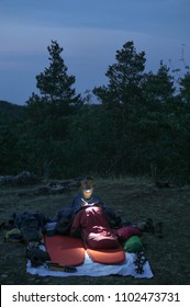 Caucasian Female Hiker Reading Book/writing Journal At Night While Wildcamping, Strong Light From Headlamp