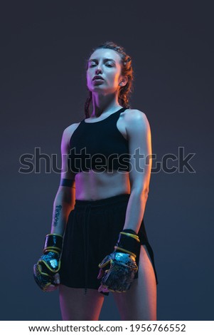 Caucasian female MMA fighter posing isolated over blue background in neon light