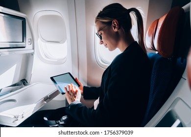 Caucasian female passenger reading eBook during international flight in business class of jetliner, successful woman using wifi internet connection on board for watching movie during free time