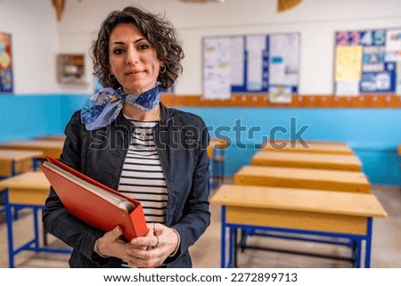 Caucasian female portrait of young teacher in class looking at camera, wearing a dark jacket and scarf. She has brown short curly hair. Educational background with copy space. Back to school concept. ストックフォト © 