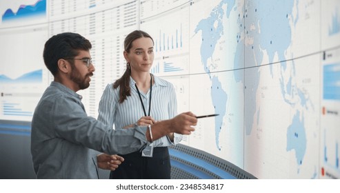 Caucasian Female Regional Manager Talking To Indian Male Distribution Expert In Front Of Big Digital Screen With Infographics And Map. Successful Man And Woman Discussing New Markets For Expansion. - Shutterstock ID 2348534817