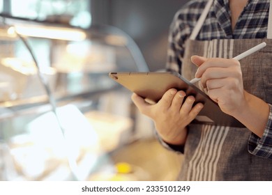 Caucasian female restaurant or coffee shop staff inspecting a bakery stock inventory in refrigerator at counter bar. Attractive female barista preparing restaurant. - Powered by Shutterstock