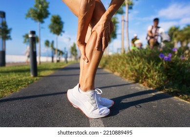 Caucasian Female Runner Sport Woman Has Leg Cramp While She Is Running On Beach In Morning. High Quality Photo