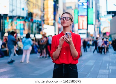 Caucasian Female Standing In Crowded Square With Mobile Phone In Hands.Addicted To Social Network. Millennial Technology User. Young Woman Browsing Internet Via App On Smartphone. Tourist Explore City