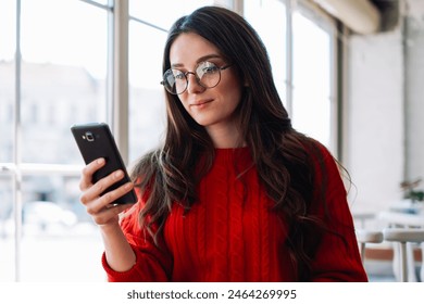 Caucasian female student checking notification and typing message using mobile phone sitting at cafeteria, attractive woman journalist waiting for interview and dialing number via cellphone indoors - Powered by Shutterstock