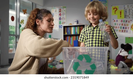 Caucasian female teacher teaching schoolkid about bottle recycle in school playroom. Little boy with teacher put plastic bottle in recycling box. Protect nature lesson  - Powered by Shutterstock