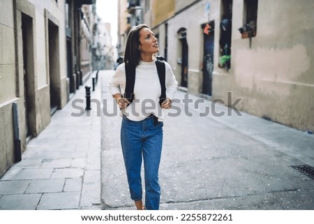 Caucasian female tourist with travel backpack walking around historic quarter enjoying solo vacations, casual dressed woman 30 years old exploring city streets during international excursion in town