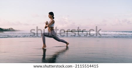 Caucasian female in tracksuit enjoying free time for training body vitality and flexibility during morning at coastline beach,slim woman stretching muscles during yoga practice for exercising in asana