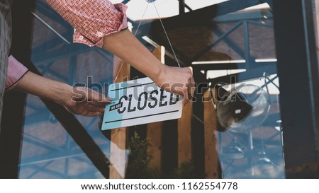 Caucasian female turning sign from open to closed on the entrance door of his small cafe. Out of business