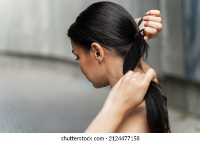 Caucasian female tying up hair at back of her head with black terry cloth ponytailer outdoors