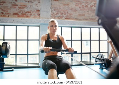 Caucasian Female Using Rowing Machine In The Gym. Young Woman Doing Cardio Workout In Fitness Club.