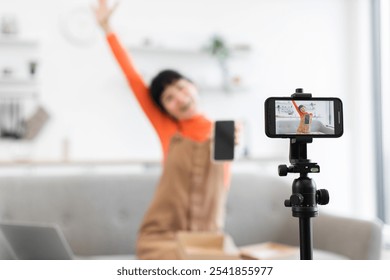 Caucasian female vlogger enthusiastically unboxing smartphone in front of camera. Young woman showcasing new gadget while sitting on sofa. - Powered by Shutterstock