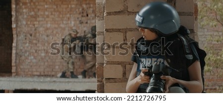 Caucasian female war journalist wearing protective helmet and bulletproof vest gear taking photos during military operation