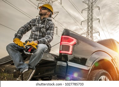 Caucasian Field Worker With Tools. Caucasian Men Wearing Safety Gloves And Hard Hat Seating On The Back Of His Pickup Truck. Contractor In The Field