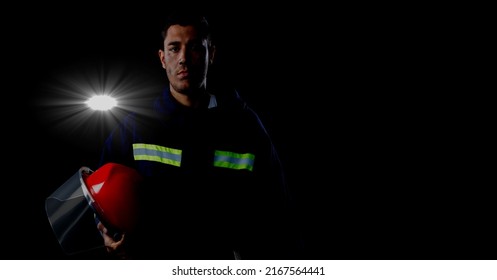 Caucasian Firefighter Holding A Helmet Against Spot Of Light And Copy Space On Black Background. Safety Concept