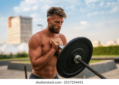 Caucasian fit man performing a barbell shoulder press exercise outdoors. He is shirtless and focused, with a cityscape in the background. - Powered by Shutterstock