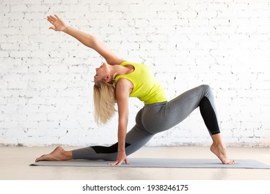 Caucasian Fit Woman Does Stretching In Deep Lunge On A Mat In Loft White Studio Indoor, Back Bending And Hip Joint Mobility, Selective Focus.