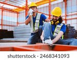 Caucasian foreman using walkie-talkie to contact safety team for help while co-worker had a steel frame crush his leg at industrial factory.